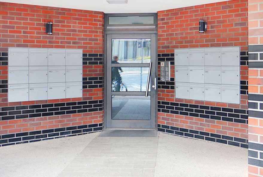 Auf beiden Seiten der Eingangstür flächenbündig an der Wand montierte zweigeteilte Briefkastenanlagen